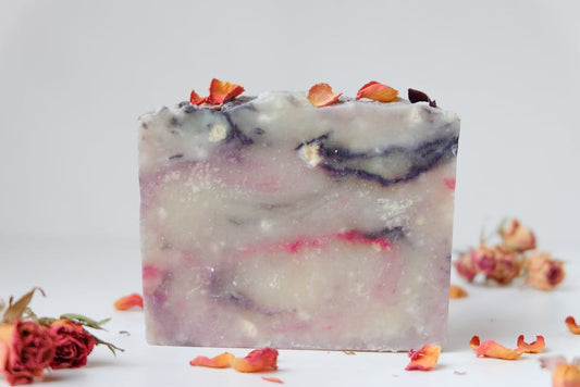 A close-up of a handmade organic soap bar with colorful swirls and dried rose petals on a white background.